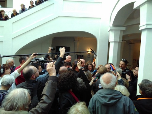 Numerous journalists surrounding Antoine and his lawyers, with boom mikes and cameras