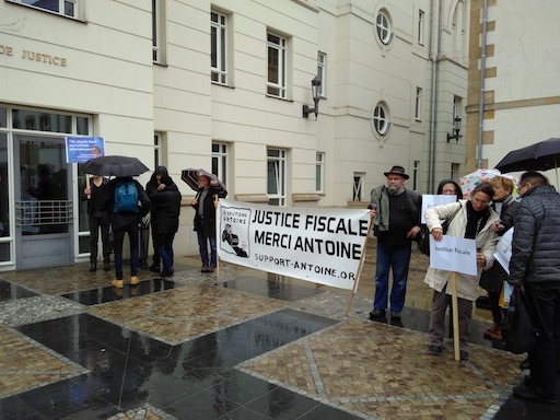 A group of supporters holding a banner, in the rain, in front of the courthouse
