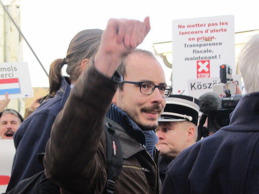 Antoine, se retournant pour saluer ses soutiens, main droite levée et souriant, en arrivant sur le parvis du tribunal